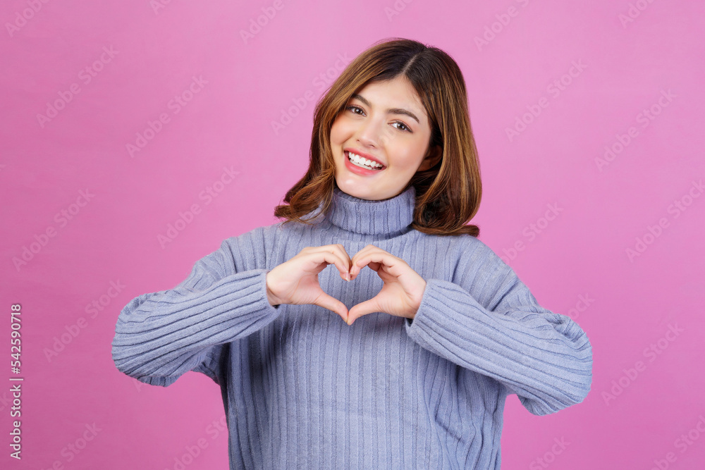 Portrait of Smiling young woman feels happy and romantic shapes heart gesture isolated over pink background Portrait of Smiling young woman feels happy and romantic shapes heart gesture isolated over pink background