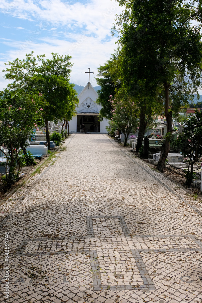 Cobbled tree lined pathway leading to Catholic chapel with crucifix cross in Santa Cruz cemetery in capital city of Dili, Timor Leste, Southeast Asia 