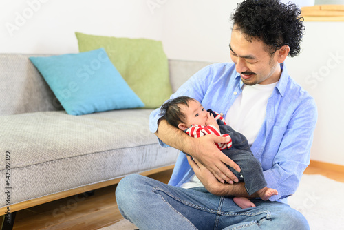 Asian bearded dad with baby in his arms and happily nursing it.	