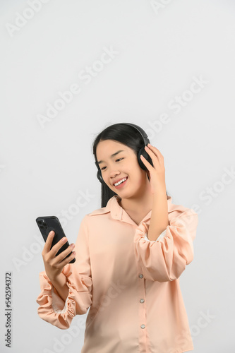 Portrait of Young asian woman with headphone listening to music and using mobile phone isolated over white background