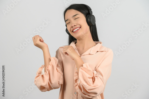 Portrait of young asian woman enjoying listening to music with large headphones in studio isolated on white background