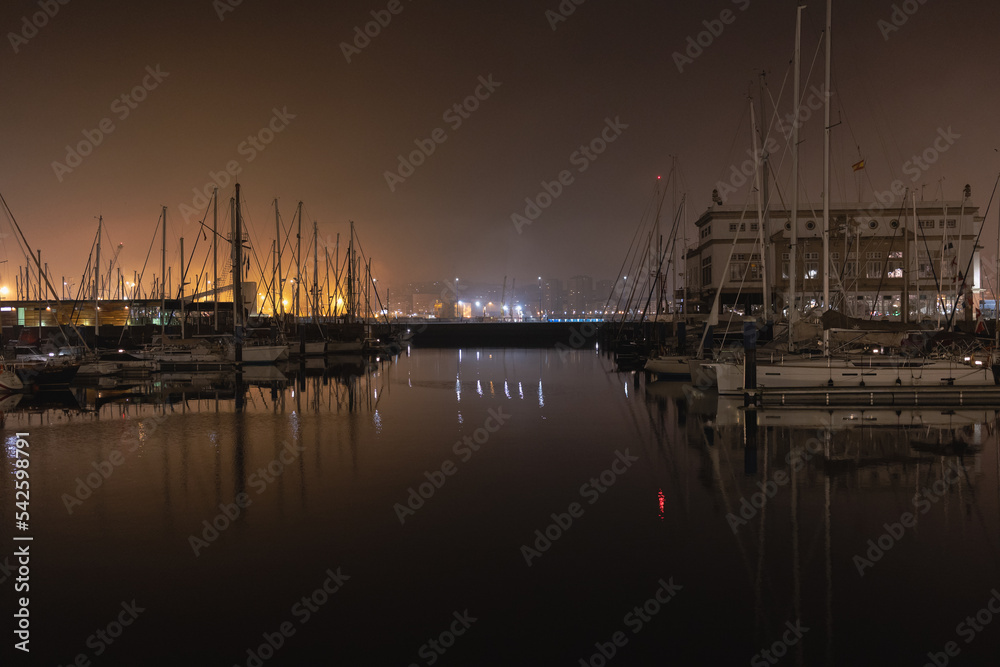 Moored yachts in the port at night in the fog. Illumination with lights and reflection of them in the water.