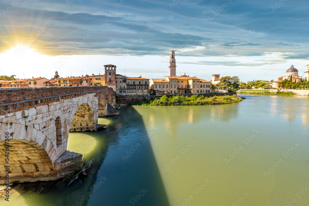 Sunset view of the Ponte Pietra bridge over the Adige River with the Torre dei Lamberti Tower rising above the old town in Verona, Italy.
