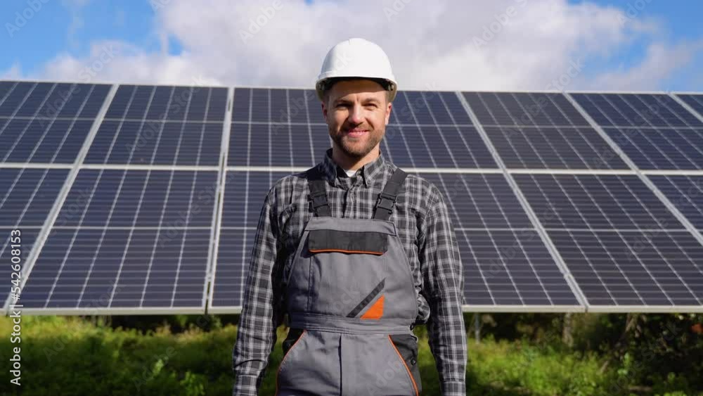 Male engineer in helmet with tools coming to the camera and smiling against the background of solar panels Male engineer in helmet with tools coming to the camera and smiling against the background of solar panels