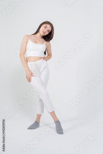 Young beautiful brown-haired girl in a white top and trousers posing on a white background