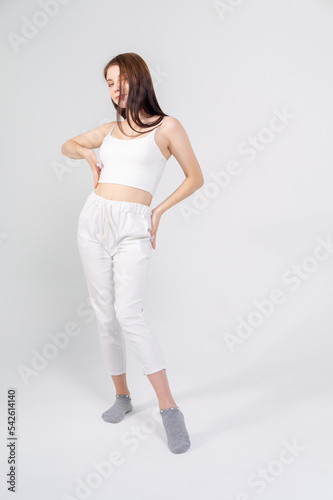 Young beautiful brown-haired girl in a white top and trousers posing on a white background