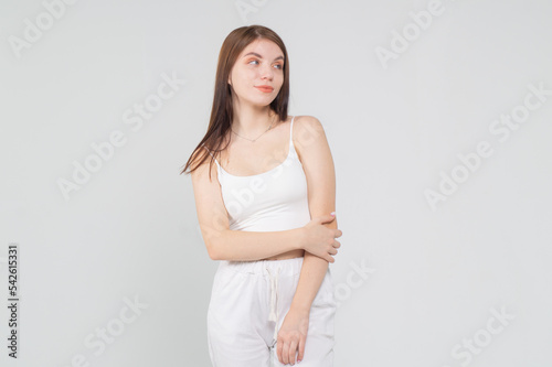 Half-length portrait of a beautiful young brown-haired girl in a white top and trousers on a white background