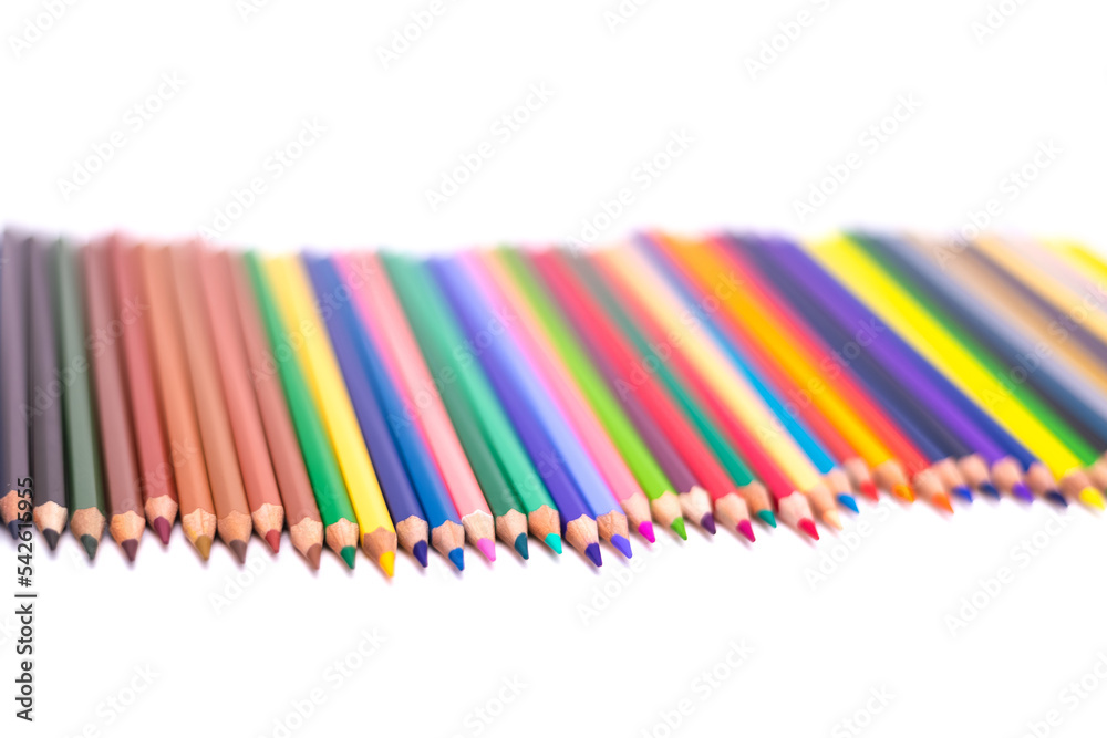 Colored pencils arranged in a curved line on a white background with a blurred background Colored pencils arranged in a curved line on a white background with a blurred background