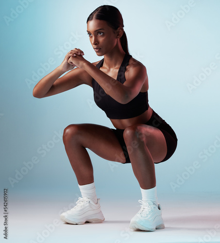 Exercise, sports and fitness model in studio doing a squat workout with motivation in sportswear. Strong, sport and slim woman athlete from India training for health while isolated by blue background photo