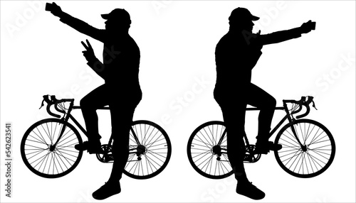 A cyclist takes a picture of himself while riding a bike. A young big guy in a cap sits on a bicycle frame, shows a victory gesture with one hand, holds a phone in the other, and takes a picture.