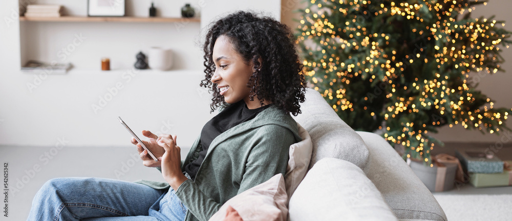 © kite_rin - Young woman using smartphone at home during Christmas holiday. Student girl texting on mobile phone banner. Communication, connection, online shopping, winter lifestyle concept