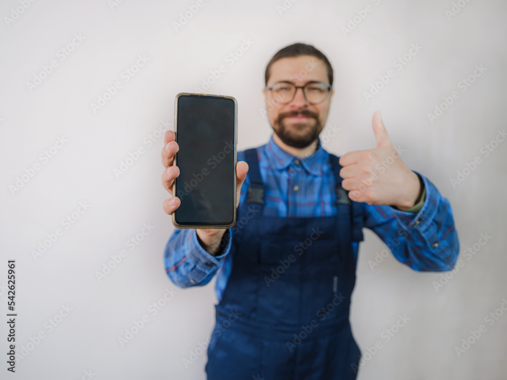 young man in blue work suit doing Repair apartment. Home renovation concept. Guy with smartphone. shows phone screen, mockup young man in blue work suit doing Repair apartment. Home renovation concept. Guy with smartphone. shows phone screen, mockup