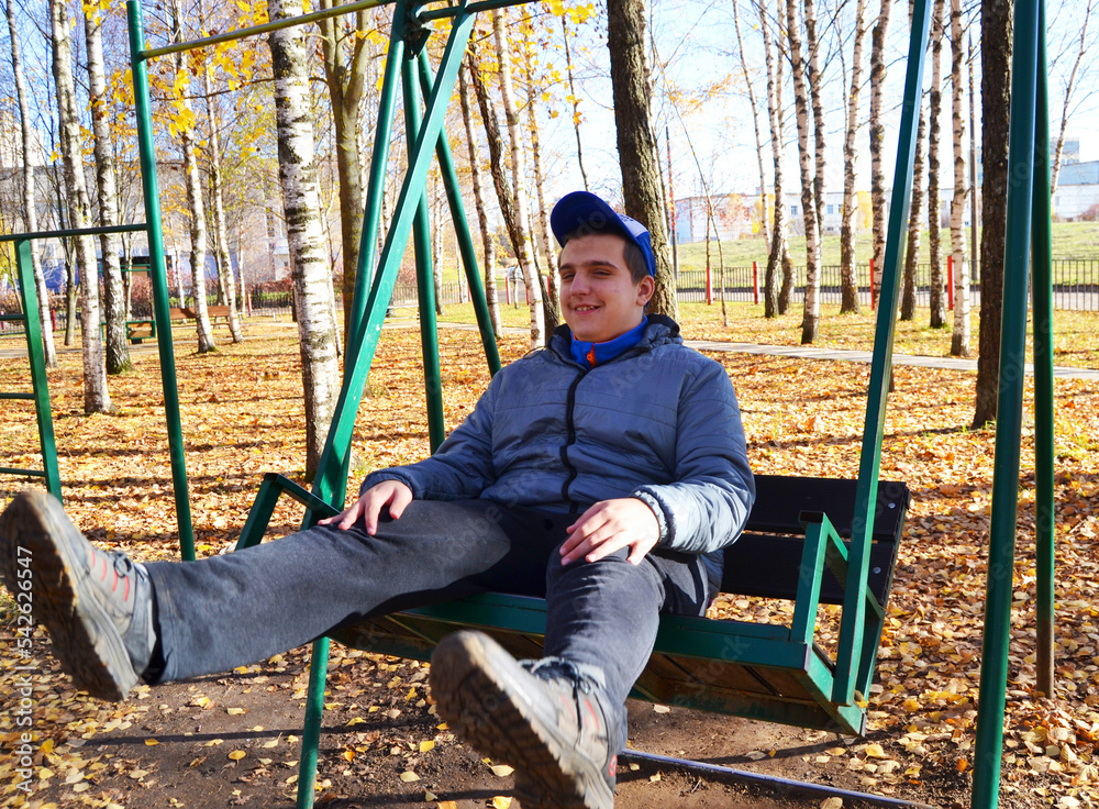 A young autistic guy rides a swing in a park - obrazy, fototapety, plakaty 