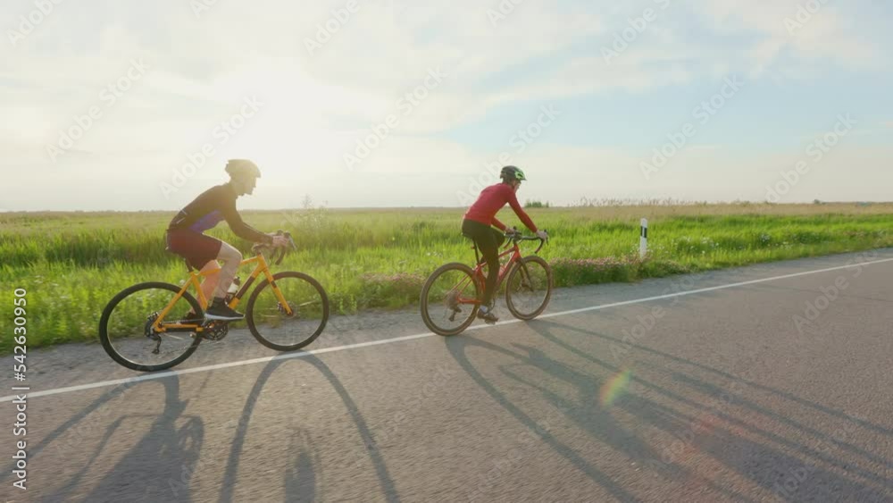 Caucasian racing bicyclists riding during intensive training along paved road. Two men in activewear and helmets preparing for cycling international competitions. Caucasian racing bicyclists riding during intensive training along paved road. Two men in activewear and helmets preparing for cycling international competitions.