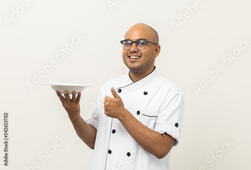 Smiling Young handsome asian man chef in uniform holding empty plate delicious dish menu good taste on isolated. Cooking indian man Occupation chef or baker People in kitchen restaurant and hotel.