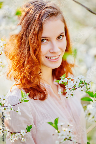 Young beautiful red-haired woman in blooming garden (selective DOF)
