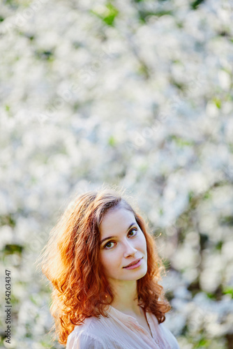Young beautiful red-haired woman in blooming garden (selective DOF)