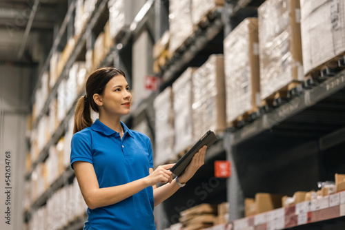 Young female worker in blue uniform checklist manage parcel box product in warehouse. Asian woman employee holding tablet working at store industry. Logistic import export concept.