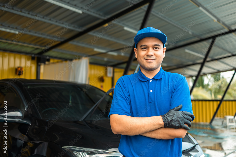 Man worker in uniform washing standing front car service station. Car