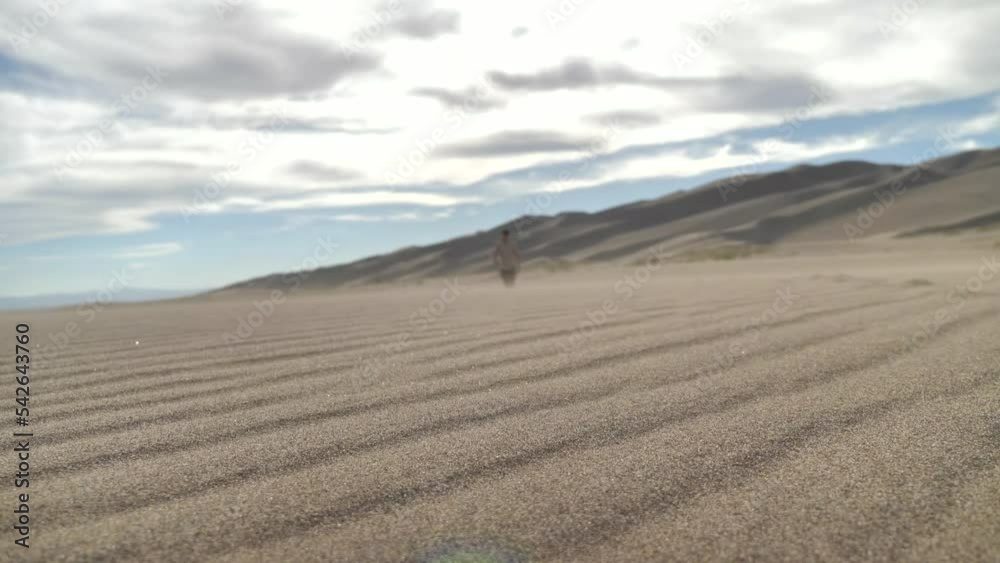 Wide Cinematic Shot of Sand Blowing While Blurred Traveler Approaches