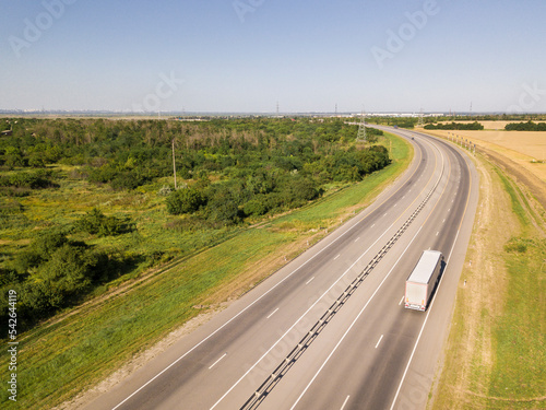 white truck driving on asphalt road along the green fields. seen from the air. Aerial view landscape. drone photography. cargo delivery
