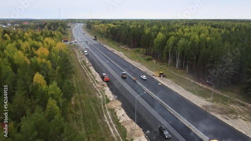 Drone top view of the road machinery. Road section repair. Laying asphalt on a forest section of an intercity highway. Steam rises over the warm asphalt pavement. Improvement and repair of driveway