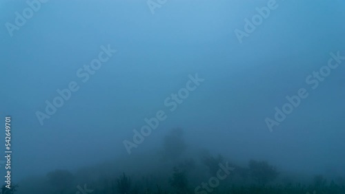 The timelapse captures the mountain covered in thick blanket of fog under floating clouds moving towards the Himalayan range, later the fog clearing up, revealing the entire near and distant hills.   photo