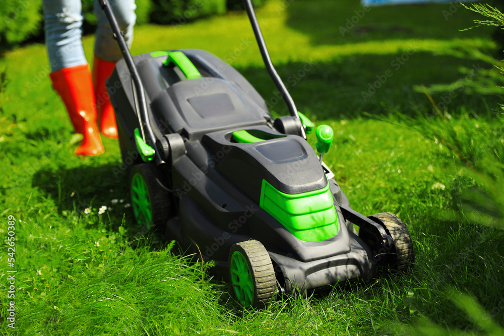 Woman cutting grass with lawn mower in garden on sunny day, closeup Woman cutting grass with lawn mower in garden on sunny day, closeup