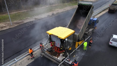 Repair of the roadbed and asphalting of the highway. The work of the asphalt paver and road workers close-up. The asphalt is added from a dump truck or a material transfer unit into the paver's hopper