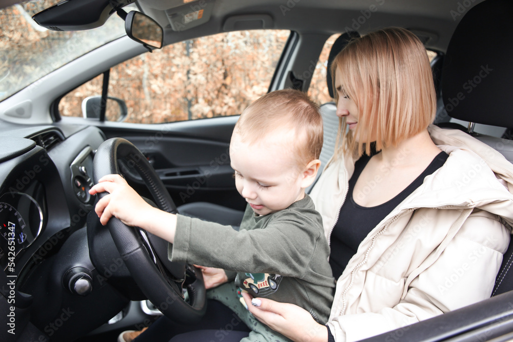 A small child sits in his mother's arms holding the steering wheel. Children in the car. Love little boys machines