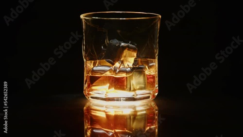 Whiskey in glass with chilling stones on black background rotating on mirror table. photo