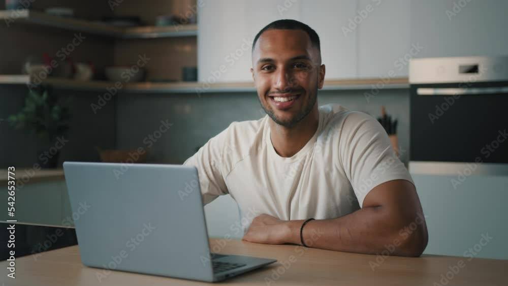 Smiling African millennial man guy American male user freelancer at home kitchen finish distant work with laptop satisfied with computer app online website networking shopping looking at camera smile