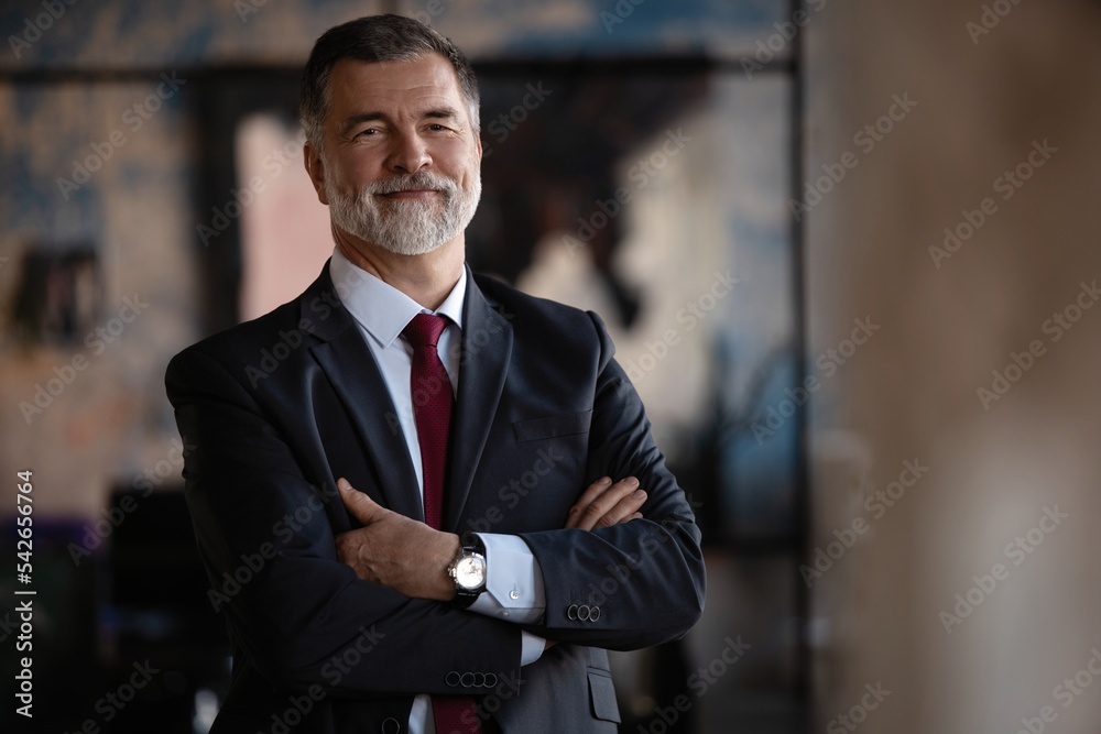 Confident mature business man with arms crossed looking at camera, smiling standing in modern office Confident mature business man with arms crossed looking at camera, smiling standing in modern office