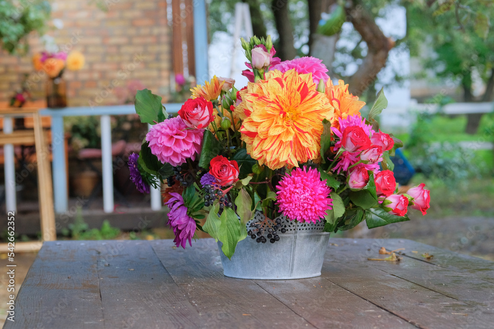 Autumn flowers: roses, asters, dahilia in the garden on a wooden table. Bright rural design. Sunny day.