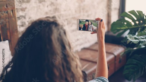 Dark-haired woman is talking to female friends online with smartphone, girl is looking at screen, holding device and talking. Focus on smart phone screen.