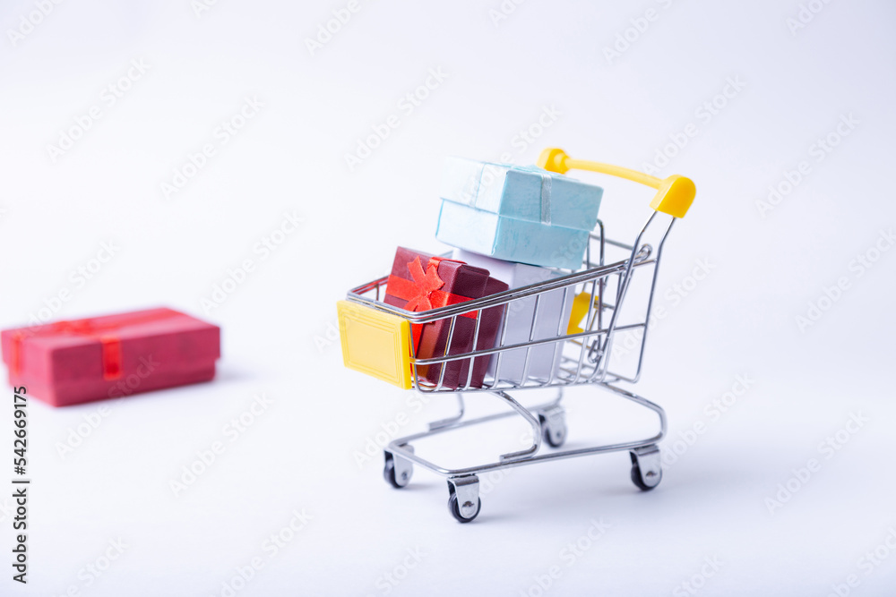 Miniature cart with gifts on a white background. Holidays shopping concept. Close-up.