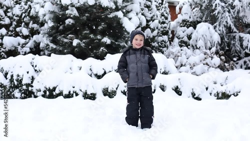 Cute young boy in winter clothes is playing with snow on back yard. Winter time