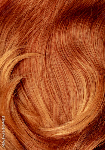Red hair close-up as a background. Women's long orange hair. Beautifully styled wavy shiny curls. Hair coloring bright shades. Hairdressing procedures, extension.