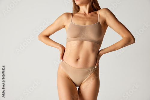 Cropped image of slim female body, breast and belly over grey background. Woman's health care