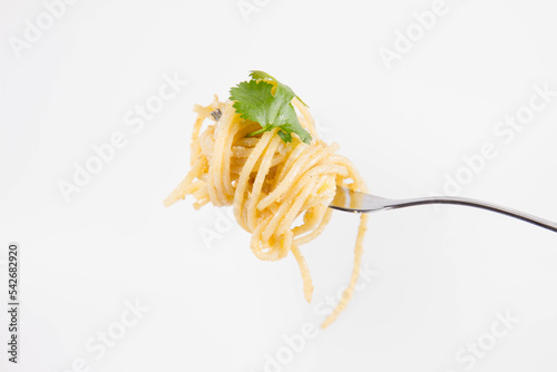 Yellow pepper pesto spaghetti covered with grated mozzarella cheese decorated with coriander rolled around a fork