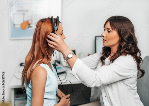 Audiologist doing impedance audiometry or diagnosis of hearing impairment. An beautiful redhead adult woman getting an auditory test at a hearing clinic.
