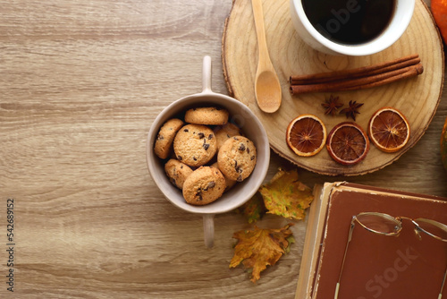 Cup of tea or coffee, seasonal spices, bowl of cookies, blanket, pumpkins, colorful leaves, books and tangerines on wooden table. Cozy hygge at home. Top view.