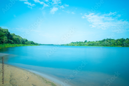 Wide river in the countryside with forest. Water surface and sandy shore in wilderness.