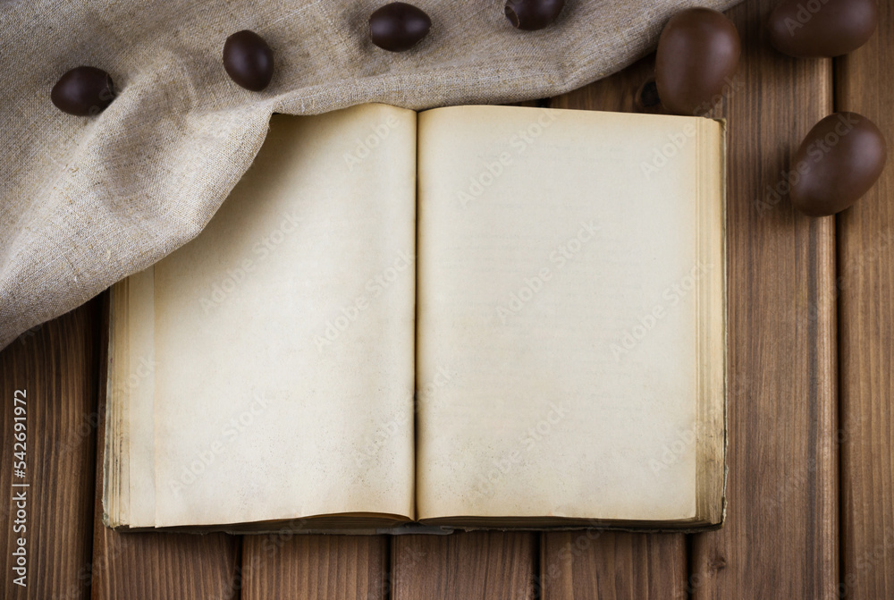 Fototapeta premium Top view of blank old book with vintage pages and chocolate eggs in the sackcloth on wooden background