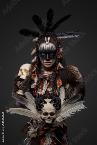 Studio shot of fearful witch woman dressed in plumed attire holding staff.