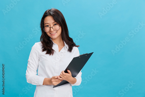 Friendly cute Asian businesswoman in classic office dress code holds folder tablet with applicant questionnaire posing isolated on blue studio background. Cool business offer. Great career concept