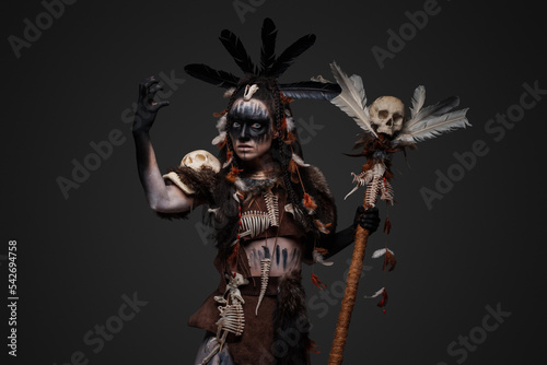 Portrait of spooky voodoo witch dressed in dark clothes holding staff with skull.