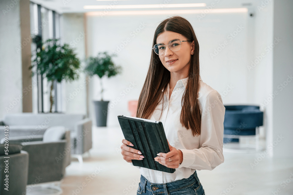 With digital tablet in hands. Young woman in glasses and in formal wear is indoors With digital tablet in hands. Young woman in glasses and in formal wear is indoors