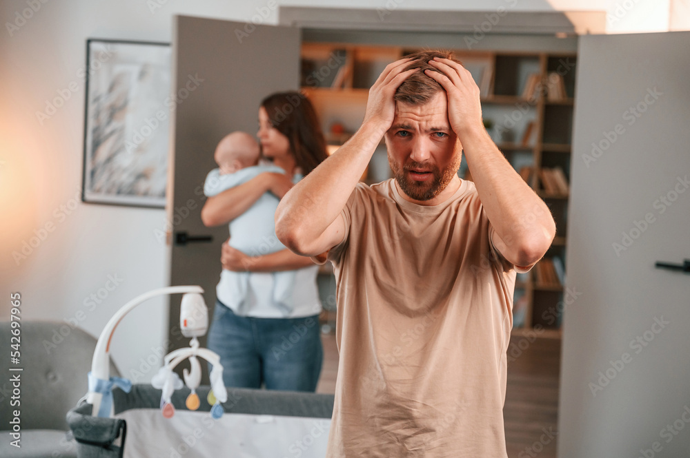 Having a headache. Conception of stress. Couple with newborn baby is at home having conflict Having a headache. Conception of stress. Couple with newborn baby is at home having conflict