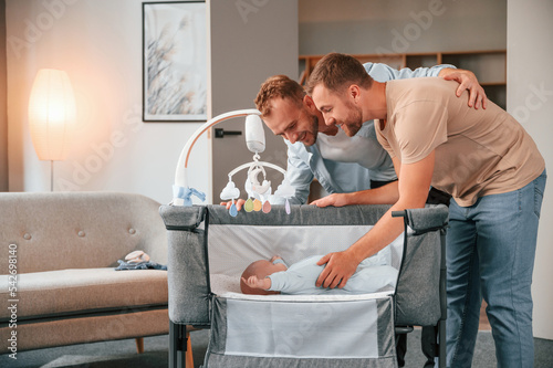 Two men is taking care of newborn baby indoors in domestic room